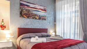 A neatly made bed with a red blanket, a cityscape painting on the wall, and a small Christmas tree on the nightstand. - Casina Rossa (Naples)