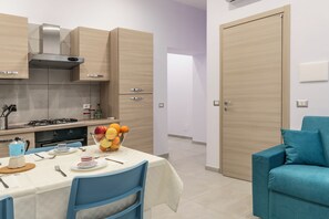 A modern kitchen with wooden cabinets, a gas stove, and a dining table set with chairs. - Casina Rossa (Naples)