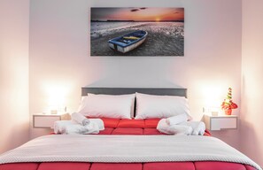 A neatly made bed with white and red bedding, a framed picture of a boat on a beach, and two bedside tables with lamps and a vase of flowers. - Casina Rossa (Naples)
