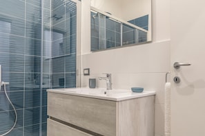 Une salle de bain moderne avec une douche à parois de verre, un lavabo blanc avec un porte-savon bleu et un meuble-lavabo en bois.
