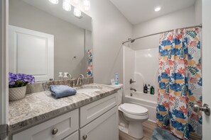 A bathroom with a marble sink, white toilet, and shower curtain with a floral pattern. - NEW! UPTOWN Cottages - 2bed/1bath - new furnishings! (Hot Springs)