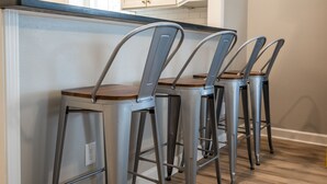 Un coin cuisine avec un comptoir-bar et trois chaises en métal dont les assises sont en bois.