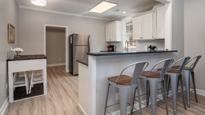Une cuisine moderne avec des meubles blancs, un réfrigérateur en acier inoxydable et un coin bar doté de tabourets en métal.