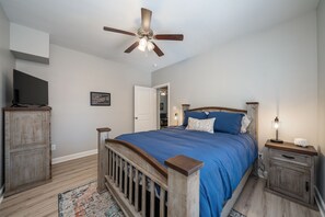 A bedroom with a wooden bed, a ceiling fan, a nightstand with a lamp, and a television on a stand. - NEW! UPTOWN Cottages - 2bed/1bath - new furnishings! (Hot Springs)