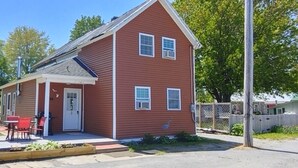 Une maison rouge à un étage, dotée d’un porche à l’avant, d’une petite terrasse et d’une cour clôturée.