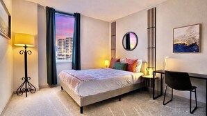 A modern hotel room with a large bed, a desk, a chair, a standing lamp, and a view of the cityscape through the window. - Wow! 5 min to DC/Metro/Mall Stunning 2B King Bed Pool Gym (Arlington)