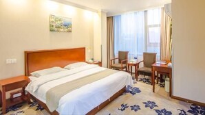 A hotel room with a double bed, a desk with two chairs, a small table, and a window with curtains. - Greentree Inn Zhonggang City Express Hotel (Jiaxing)