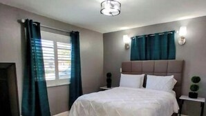 Ein Schlafzimmer mit Bett, Vorhängen, einem Nachttisch, einer Wandlampe und einem Fernseher.
