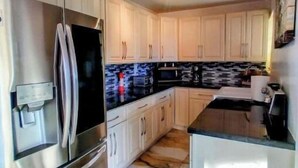 Eine moderne Küche mit weißen Schränken, einem Edelstahl-Kühlschrank und einem Marmorboden.