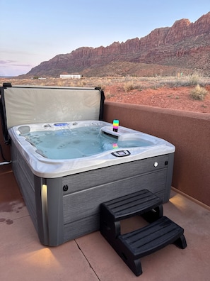 Un bain à remous doté d’un panneau de commande, d’un petit marchepied et offrant une vue sur un paysage désertique avec des montagnes.