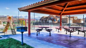 An outdoor patio area with picnic tables and a children's play structure. - "Solitude De La Sal", Private Hot Tub, Pools, Views, Sleeps 8 (Moab)