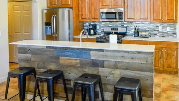 A kitchen with wooden cabinets, a stainless steel refrigerator, a microwave, a coffee maker, and a large island with stools. - "Solitude De La Sal", Private Hot Tub, Pools, Views, Sleeps 8 (Moab)