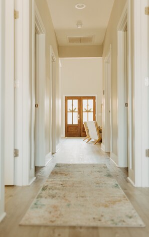 Un pasillo con una puerta de madera al final, una puerta blanca a la izquierda y otra blanca a la derecha.