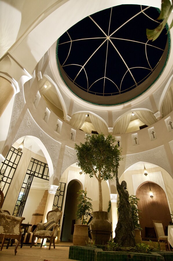 A spacious lobby with a high ceiling, a central tree, and a staircase leading to upper floors. - La Claire Fontaine (Marrakech)