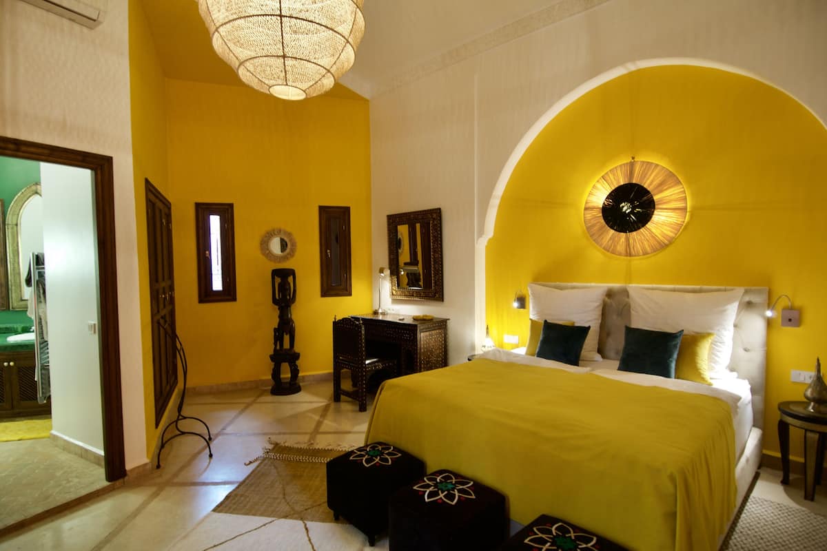 A hotel room with a large bed, a round mirror, and a unique yellow arch design.