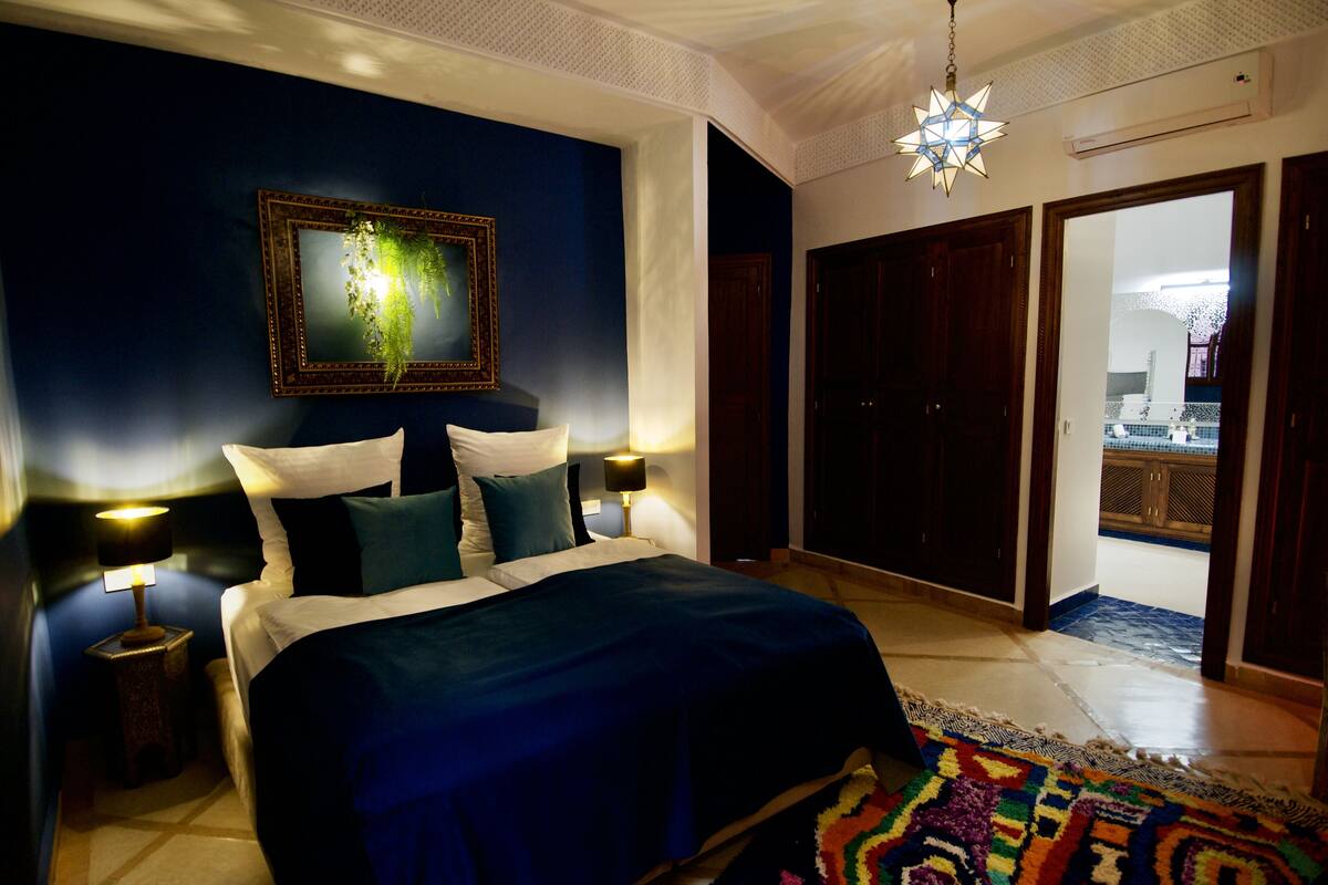 A bedroom with a large bed, two bedside tables, a nightstand, a decorative mirror, and a star-shaped hanging light fixture.