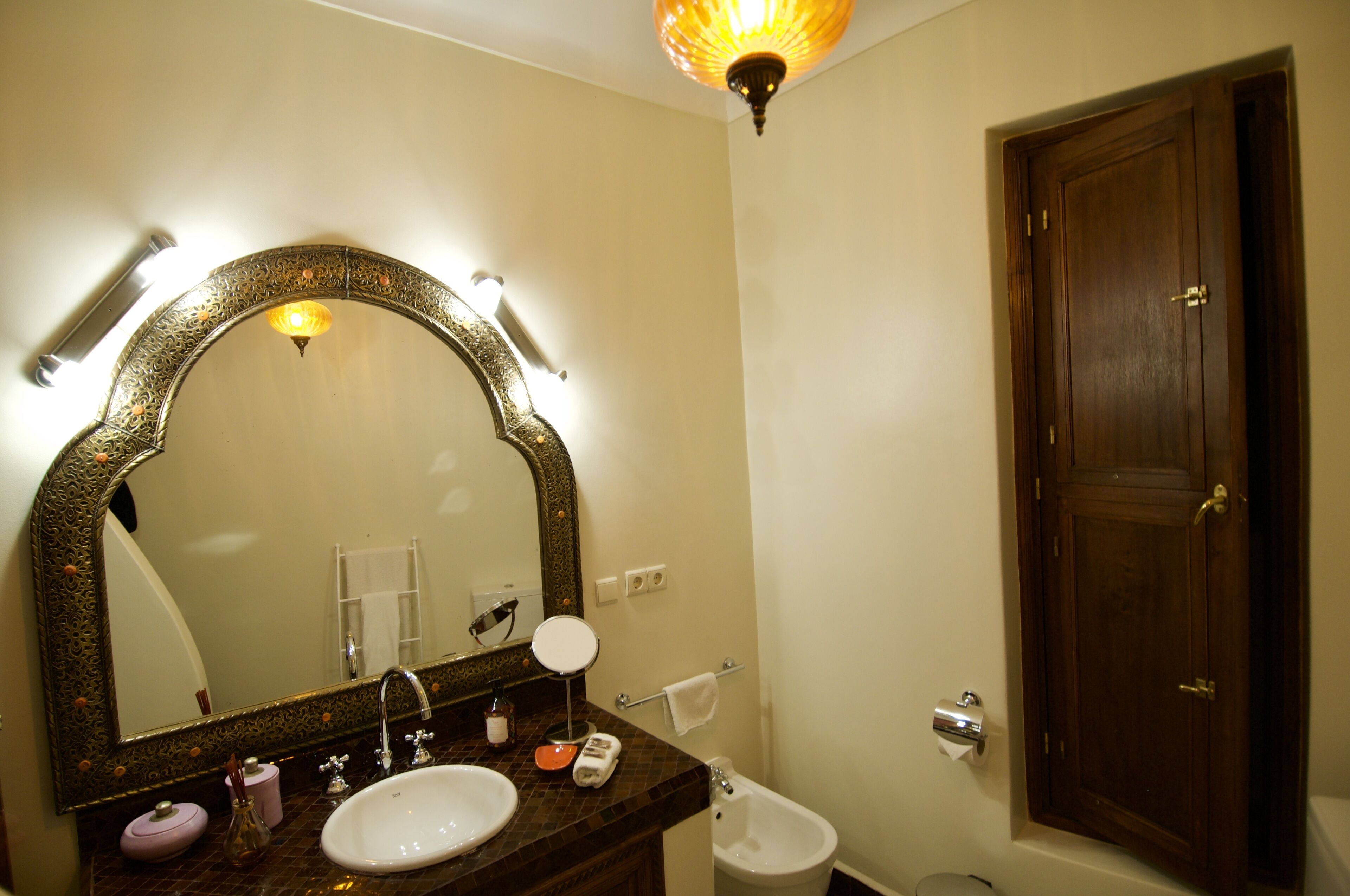 A bathroom with a large ornate mirror, a sink, a toilet, and a wooden door.