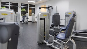 Un gimnasio con diferentes máquinas de ejercicio, un ventanal con vistas al exterior y una puerta que da a otra habitación.