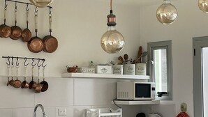 Una cocina con ollas de cobre colgando, un microondas, un hervidor y una cafetera sobre la encimera.