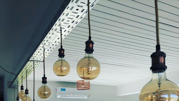 Un interior moderno con lámparas esféricas colgantes, una piscina visible a través de puertas de vidrio y una zona de estar con mesa y sillas.