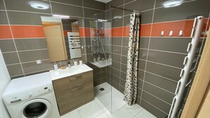 Een moderne badkamer met een wasmachine, een wastafel, een spiegel en een douche.
