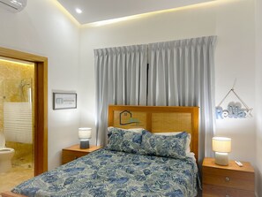 Ein Schlafzimmer mit einem Bett, Nachttischen, einer Lampe, einem Spiegel, einem gerahmten Bild und einem Vorhang.