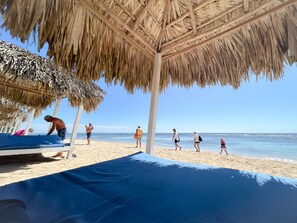 Ein Strand mit einer strohgedeckten Struktur, feinem Sand und einem klaren, blauen Himmel.