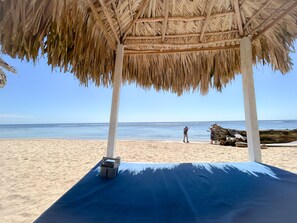 Ein Strand mit einer strohgedeckten Struktur, einer blauen Matte und einer Kamera im Sand.