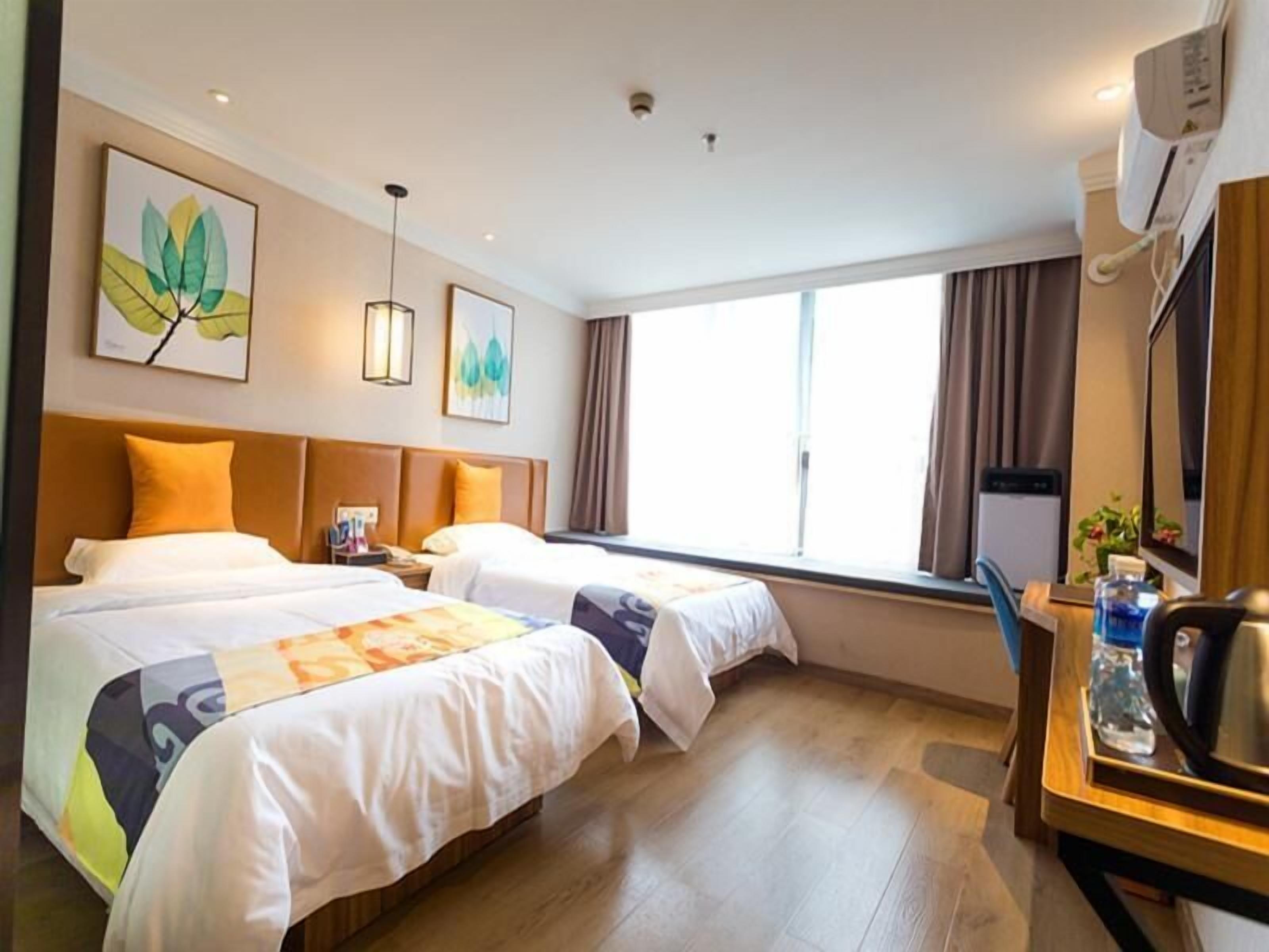 Une chambre d’hôtel avec deux lits, un bureau avec une chaise, une fenêtre et des œuvres d’art accrochées aux murs.