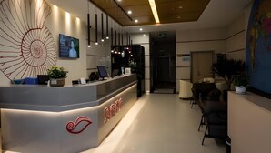 A modern reception area with a central desk, a large decorative wall piece, and a seating area with chairs.