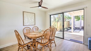 Un comedor con una mesa de madera redonda y seis sillas, un ventilador de techo y un gran ventanal corredizo que da a un patio exterior.