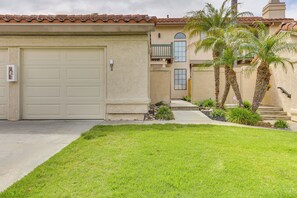 A residential building with a beige garage door, a small front yard with grass and plants, and a balcony with a railing. - Extended Stay Near Beach! Carlsbad Condo w/ Pool (Carlsbad)