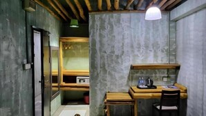 Habitació petita amb escriptori de fusta, cadira i una petita prestatgeria. Una porta condueix a una altra habitació.