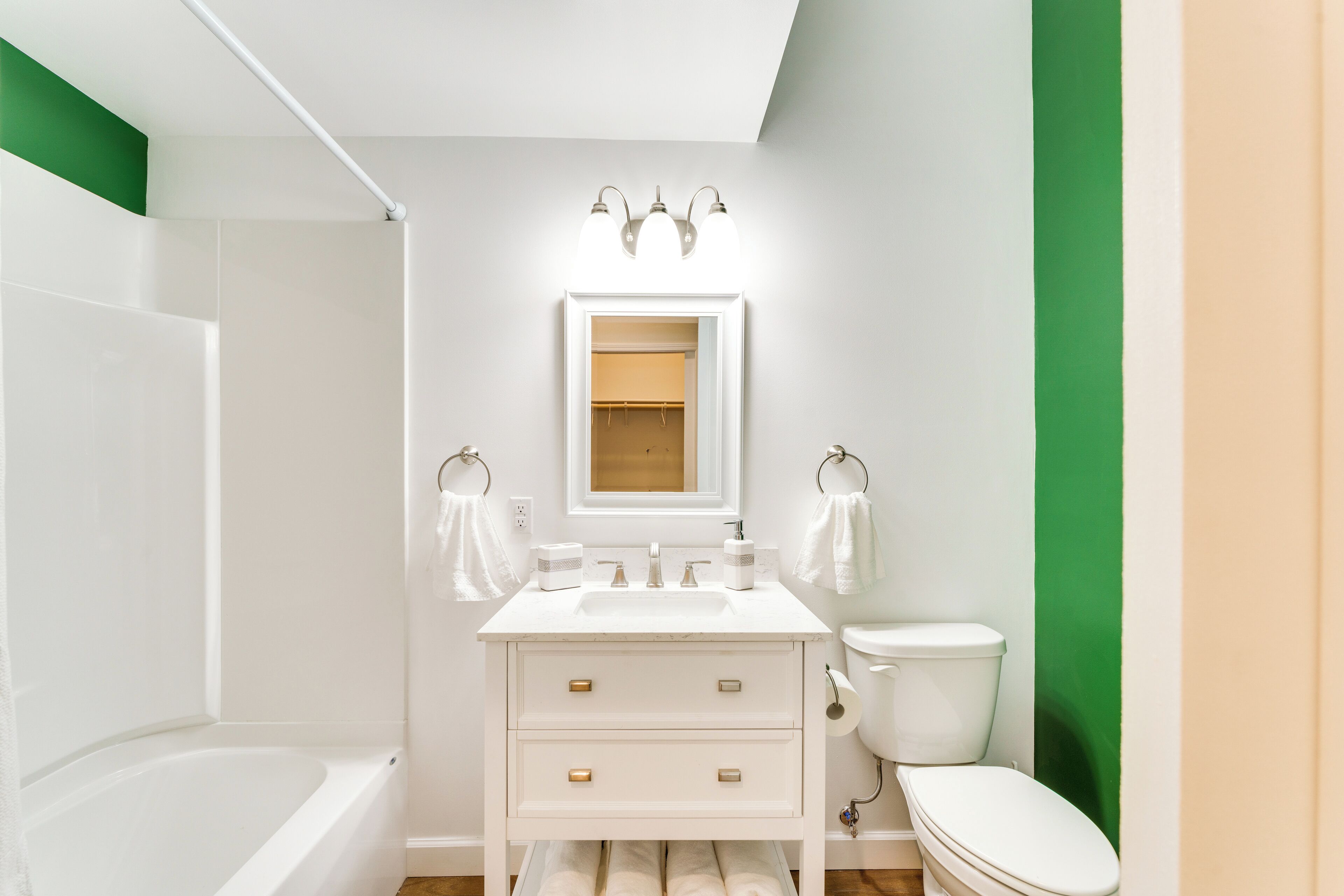 A modern bathroom with a white vanity, a bathtub, and a toilet.
