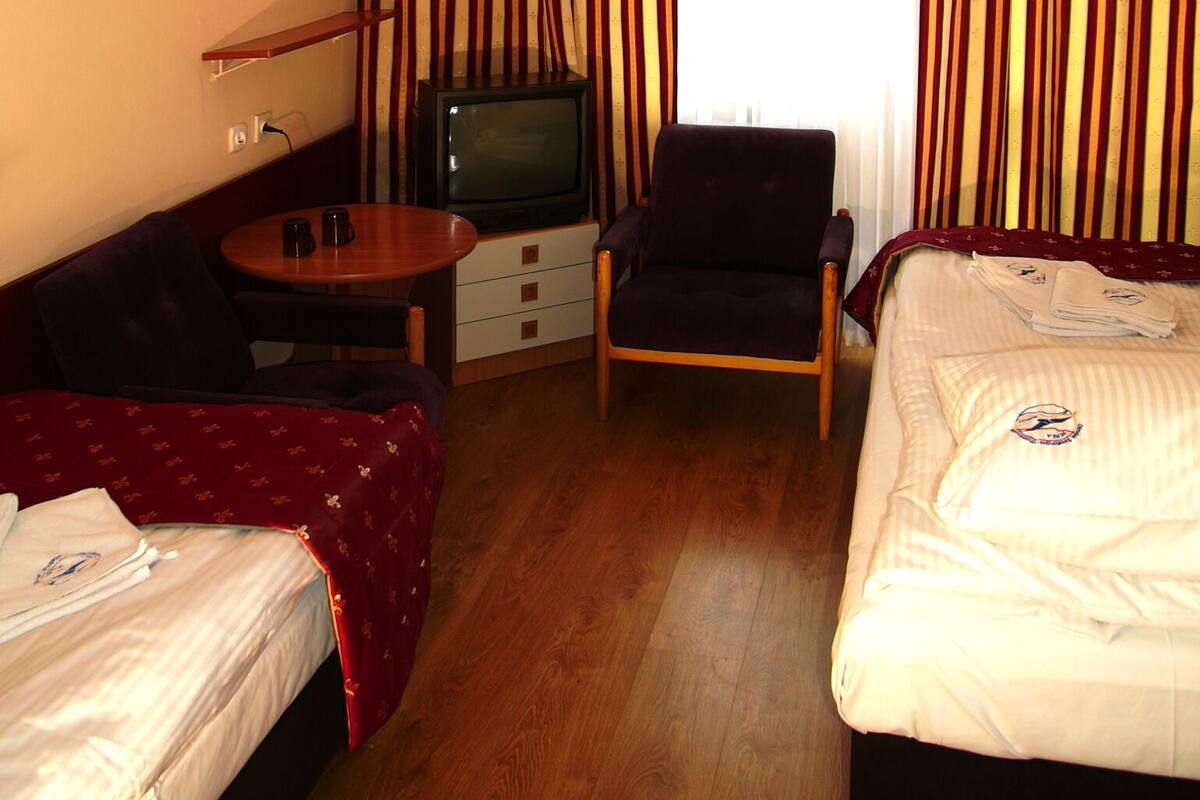 A hotel room with a bed, a chair, a small table, a television, and curtains.