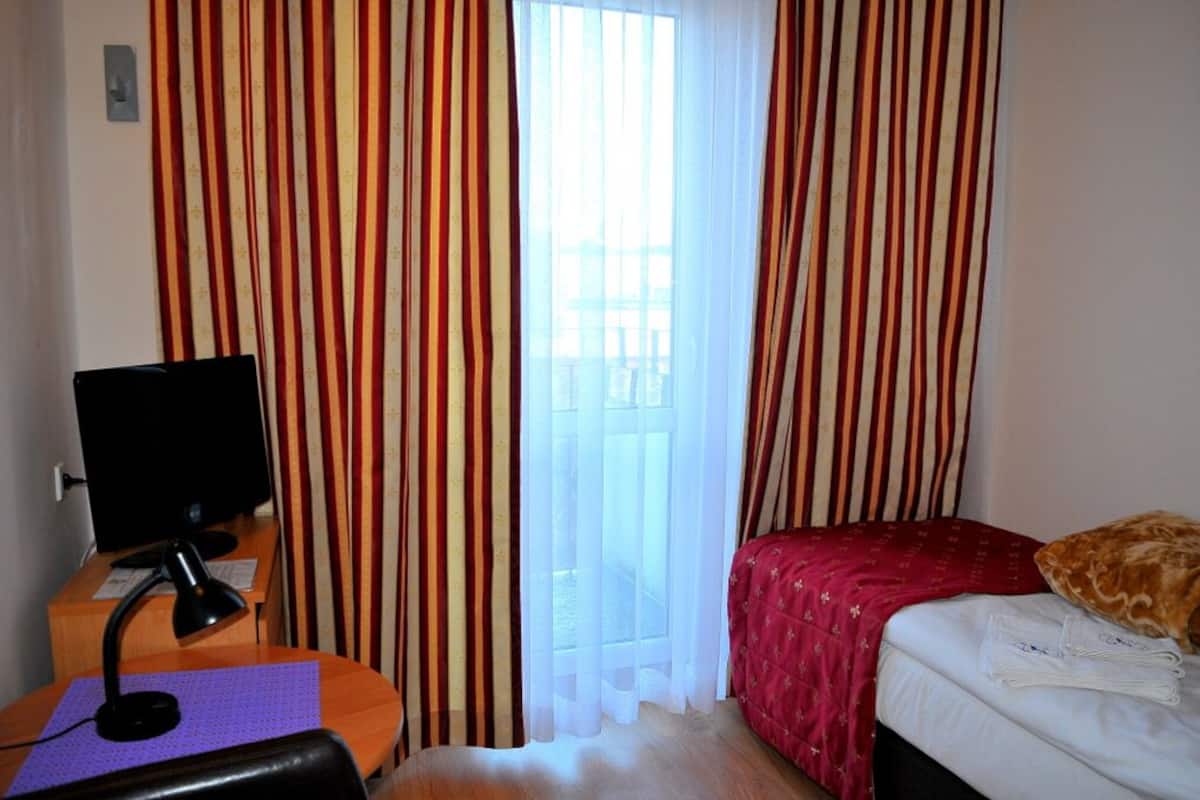 A hotel room with a bed, a desk with a computer, a chair, and curtains.