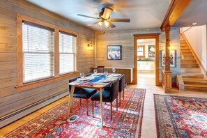 A dining area with a table set for four, wooden walls, a ceiling fan, and a staircase leading to another level.