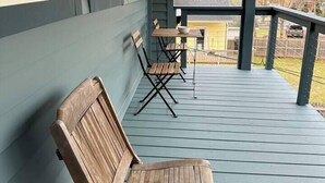 A covered porch with wooden chairs and a table, a view of a yellow house in the background, and a wooden fence. - Spacious Arts & Crafts Village Home | Perfect 4 Season Base Near Trails & Events (Margaretville)