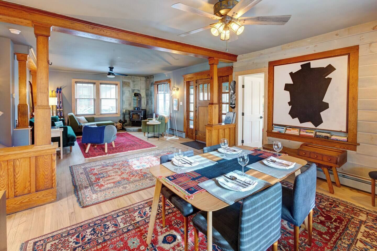 A dining area with a wooden table set for six, surrounded by patterned rugs and blue upholstered chairs.