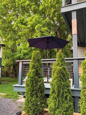 A modern outdoor seating area with a dark umbrella, surrounded by neatly trimmed evergreen trees.