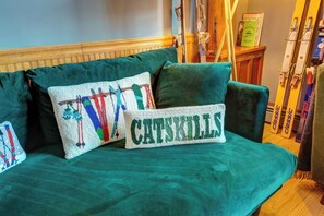 A green sofa with two decorative pillows, one with a colorful design and the other with the word 'CATSKILLS'.