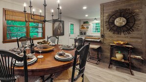 Un comedor con una mesa de madera dispuesta para cuatro personas, rodeada de sillas, una lámpara de araña y decoración rústica en la pared.