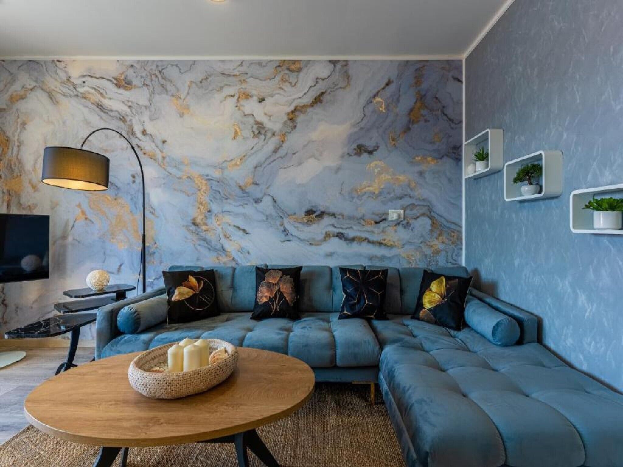 Uma sala de estar moderna com um sofá azul, uma parede de mármore, uma mesa de centro redonda de madeira e um abajur.