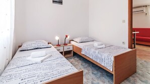 A small, clean room with two single beds, a nightstand with a lamp, and a small wall-mounted picture.