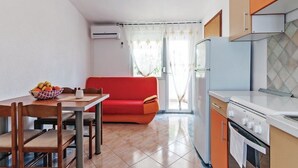 A compact kitchen with a dining area, a red sofa, and a refrigerator.