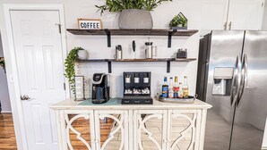 Una cocina con estación de café, refrigerador y estante con plantas.
