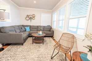 A living room with a gray sectional sofa, a round coffee table, a wicker chair, and a patterned rug.