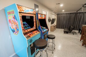 A room with two arcade machines, a TV, a couch, and a bar stool.