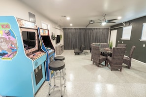 Una habitación con una máquina de videojuegos Nintendo, una mesa de comedor con sillas de mimbre y un ventilador de techo.