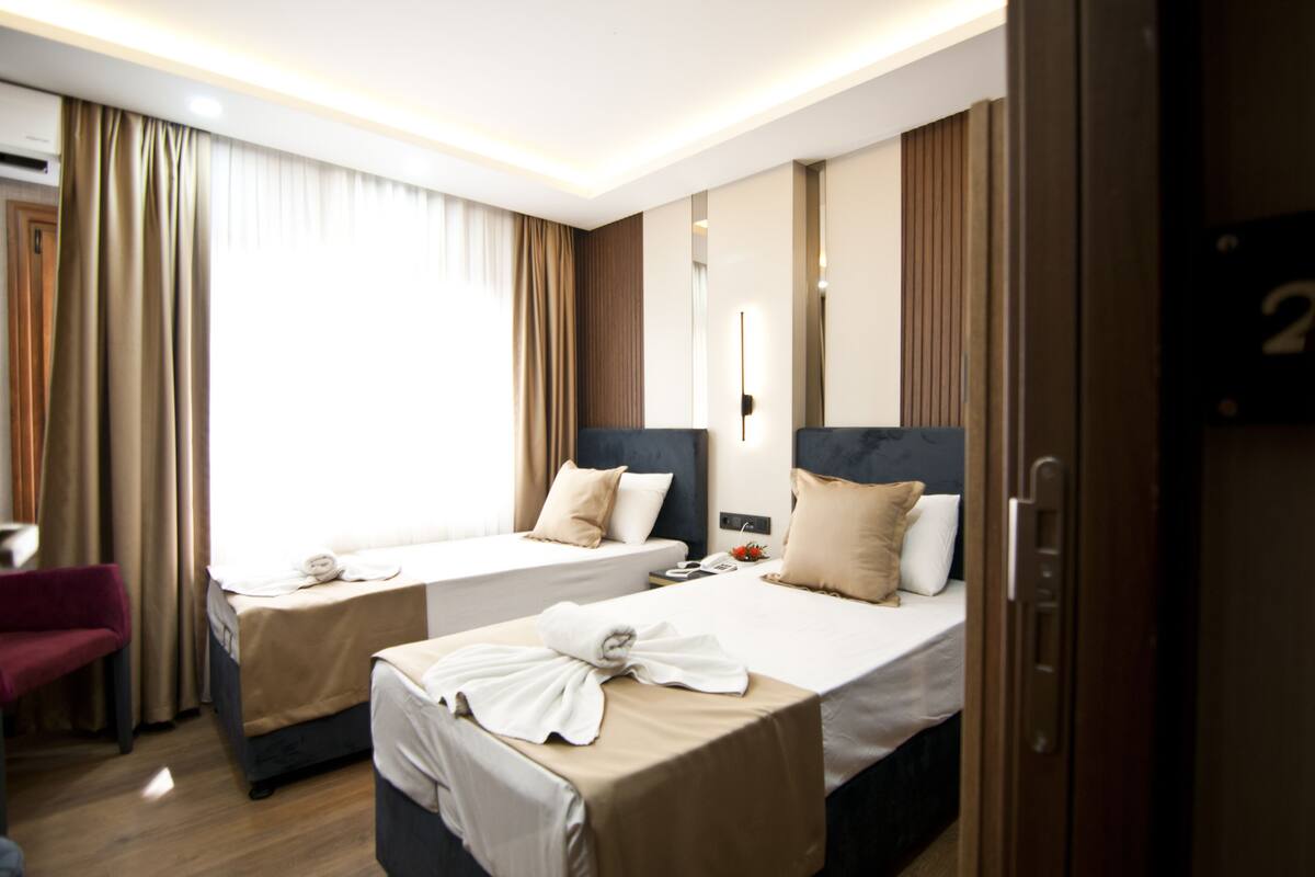 A hotel room with two beds, a red chair, and a door with a number.
